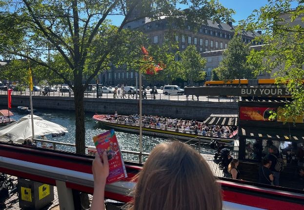 Blick von Ved Stranden auf ein vorbeifahrendes Ausflugsboot, gesehen aus einem Sightseeingbus mit Fahrgast und Karte