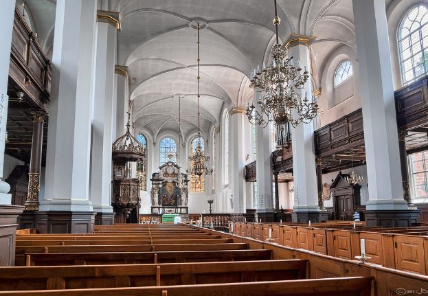 Interior of the Church of the Holy Spirit in Copenhagen with wooden pews, chandeliers, columns, and vaulted ceiling