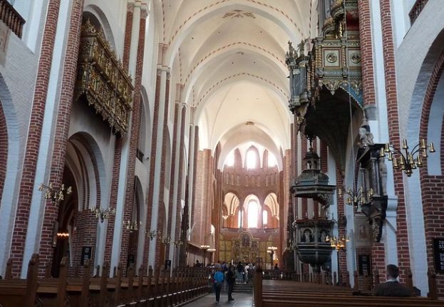 Interior of Roskilde Cathedral with brick columns, vaulted ceiling, ornate pulpit, and wooden pews