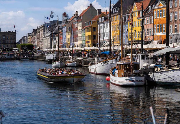 Canal boat with guests sailing along the Nyhavn canal lined with colorful houses.