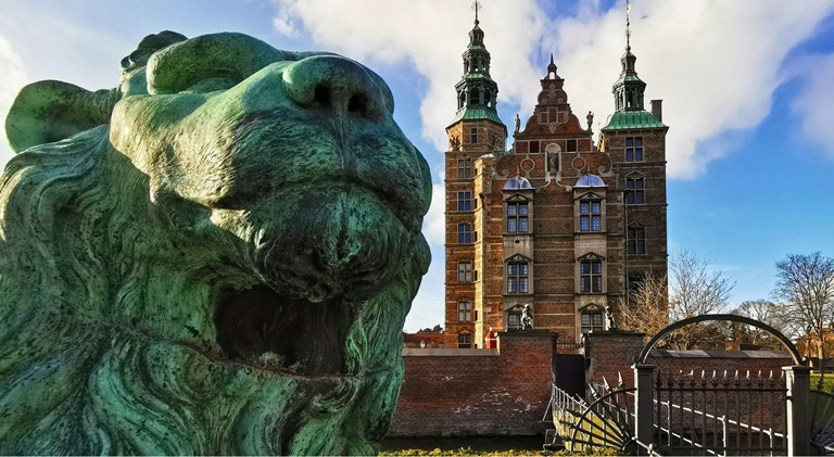 Close-up of a lion statue with Rosenborg Castle visible in the background.