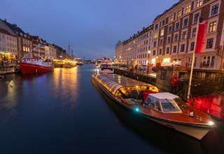 A canal boat docked at Nyhavn in the evening, surrounded by festive lights and historic buildings.
