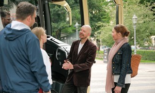 Ryhmä keskustelemassa oppaan kanssa kiertoajelubussin luona