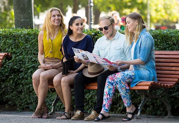 Four persons sitting on a bench in the Esplanade Park, Helsinki. They are reading a map.