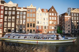 Een rondvaartboot met glazen dak vaart op een zonnige dag langs Amsterdamse grachtenpanden