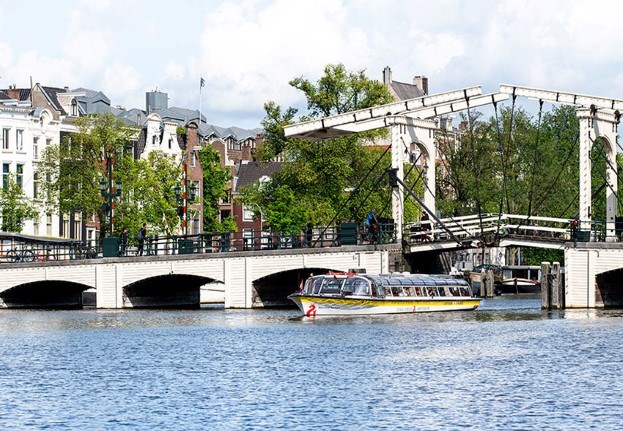 Een Stromma boot vaart door de Magere Brug met Amsterdamse huizen op de achtergrond