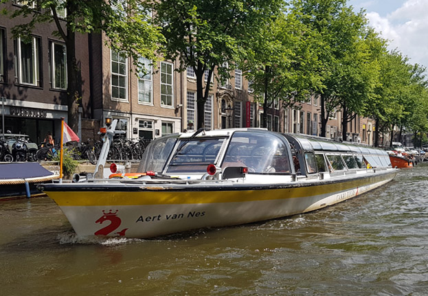 A canal cruise boat passing through an Amsterdam canal during a sunny day