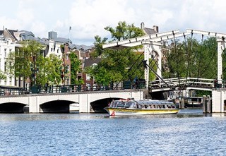 A Stromma boat sightseeing tour sailing through the Skinny Bridge with Amsterdam houses in the background