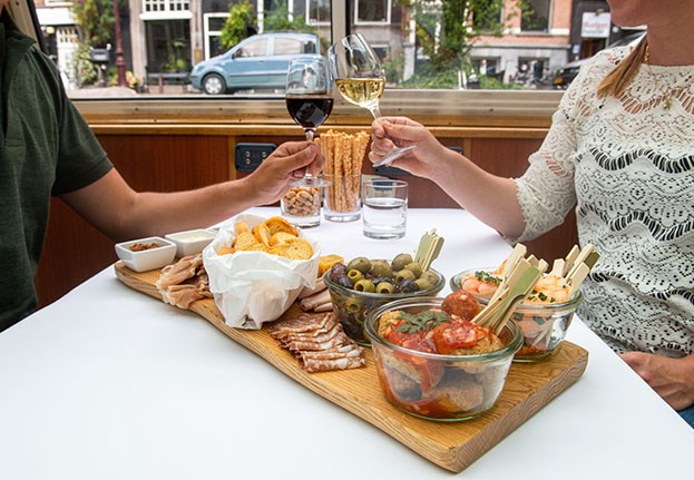 A wooden plank full with snacks and guests are holding their drink