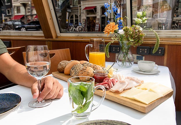 Table filled with breakfast buns and toppings, including some orange juice and tea or coffee