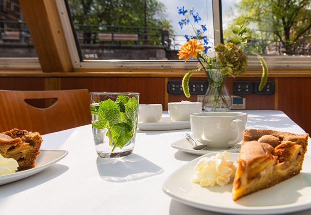 Gasten eten een Nederlandse appeltaart, thee en koffie tijdens een cruise op deze zonnige dag in Amsterdam