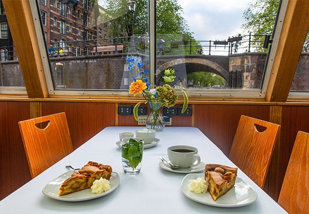 Appeltaart, koffie en thee op tafel met een uitzicht over de Amsterdamse grachten en bruggen