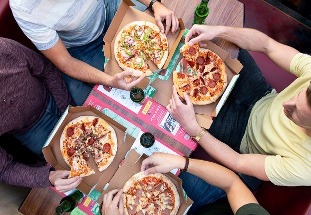 Een foto van pizza's met het zicht vanaf de bovenkant en vier gasten aan tafel