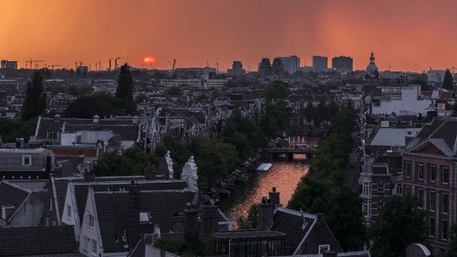 Amsterdam city skyline at sunset, with canals, historic buildings and treelined streets.