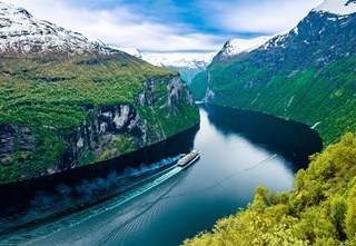 Cruise ship sailing through Geirangerfjord surrounded by steep mountains.