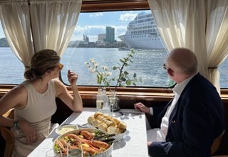 Woman and a man enjoying a crayfish meal on MS Nobel looking out on the water in the Oslofjord
