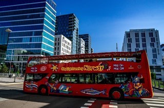 The Red Stromma City Sightseeing double-decker bus driving through the streets of Oslo with Barcode in the background