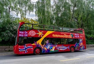 Bright red City Sightseeing Norway double-decker bus parked by a tree-lined street.
