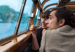 Two people looking out the window during a canal cruise, pointing at the view with interest.