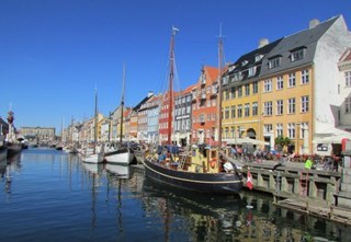 Nyhavn in Copenhagen, Denmark, lined with colorful historic buildings, boats, and outdoor cafés in sunshine.
