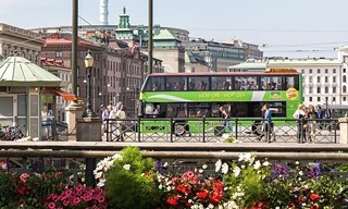 Hop-On Hop-Off-buss som passerar en blomsterkantad kaj i centrala Göteborg – stadsrundtur.