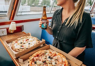Gäst med alkoholfri öl i handen framför två nygräddade pizzor ombord på båten