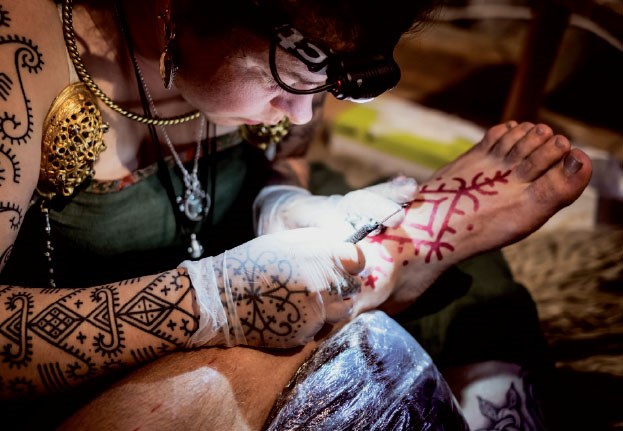A tattooed woman is tattooing a foot