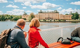 Couple on boat deck gazing at Drottningholm Palace across the water, Stockholm.