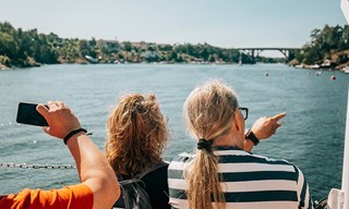 Gäster ombord båtturen Skärgårdens höjpunkter pekar mot Skurusundsbron i Stockholms skärgård.