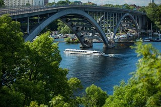 Sightseeingbåt passerar under Västerbron i Stockholm, med grönska i förgrunden