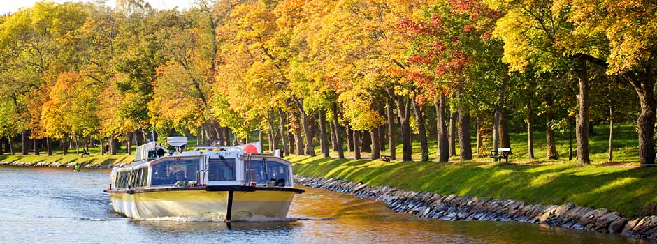 A sightseeing boat travels along the Djurgårdenskanalen, lined with yellow autumn trees