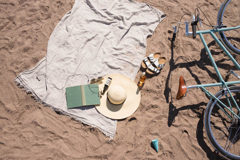 Towel, sun hat, book, bicycle and sandals lying on a sunny beach