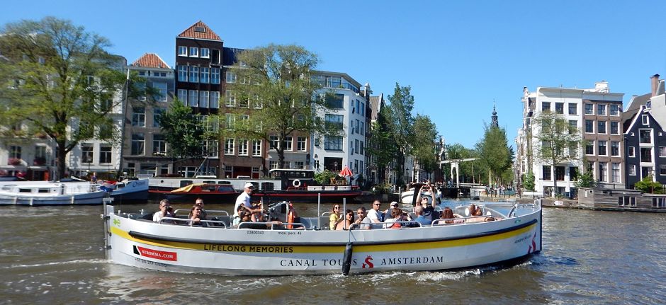 An open sightseeing boat on the canals of Amsterdam. Summer with blue sky and traditional canal houses in the background.