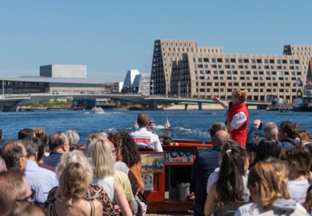 Tour guide speaking to guests on a canal boat in Copenhagen with the Paper Island in the background