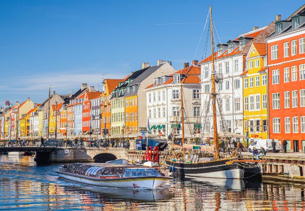 Covered canal boat sailing through Nyhavn on a sunny day. Colorful houses along the canal.
