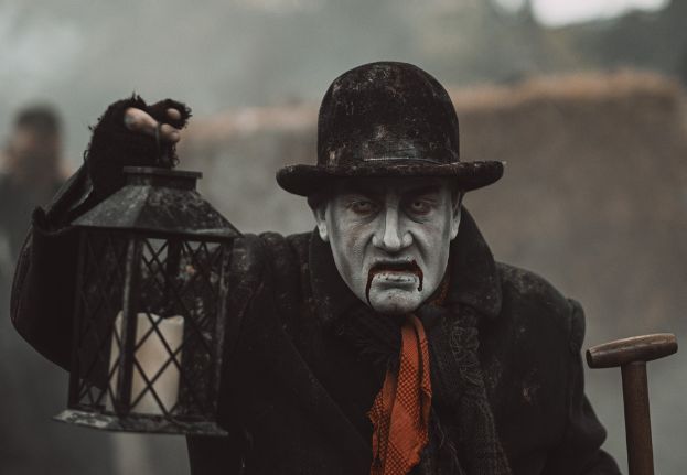 Pale and ghostlike man dressed in black and holding a lantern.