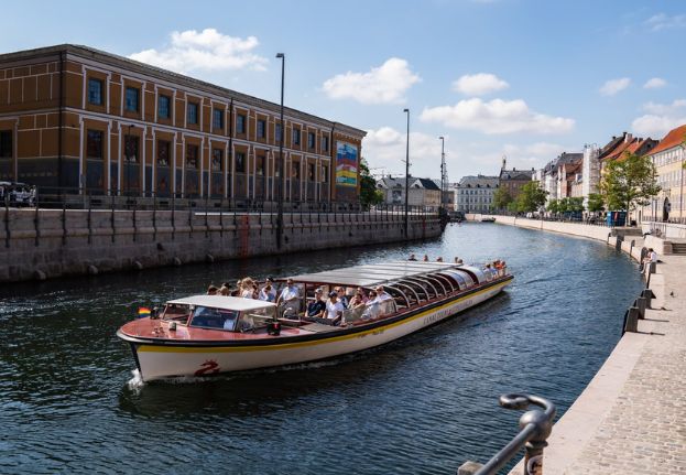 Covered canal boat with guests sailing through a narrow canl in Copenhagen.